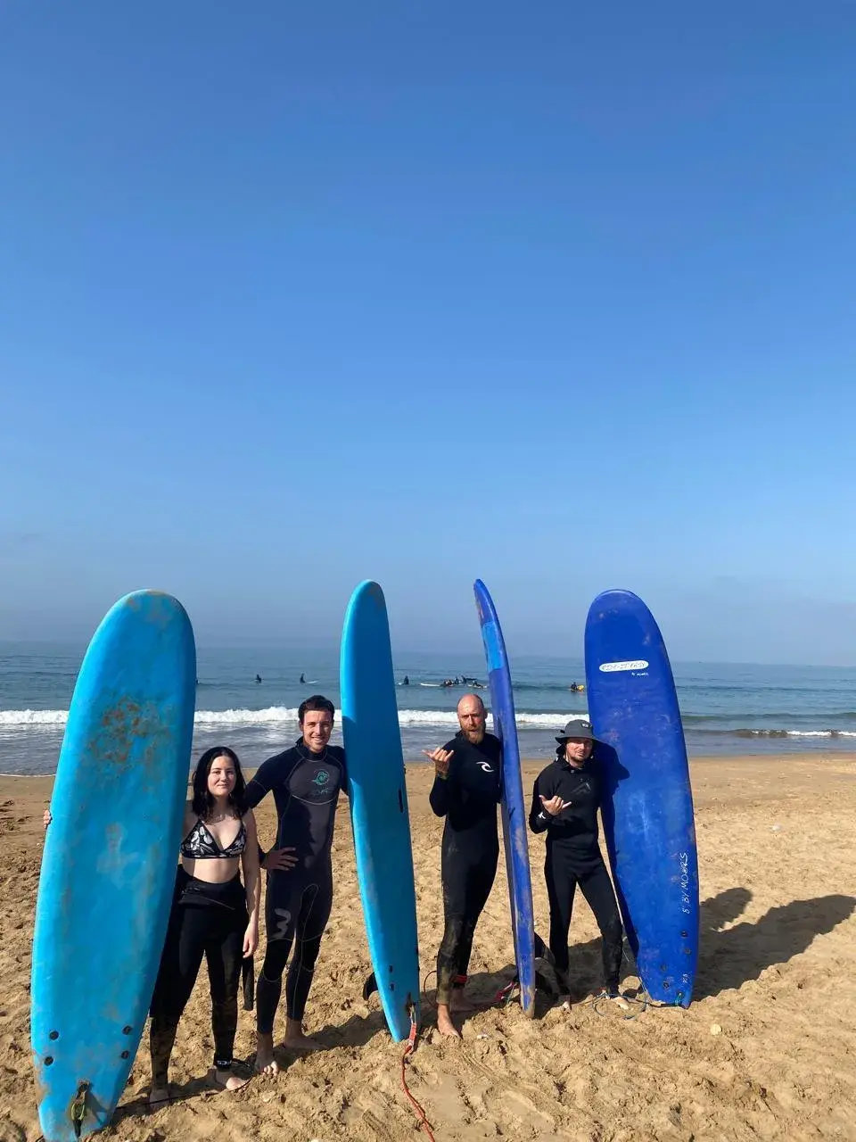 A group of surfers standing beside upright blue surfboards on the beach