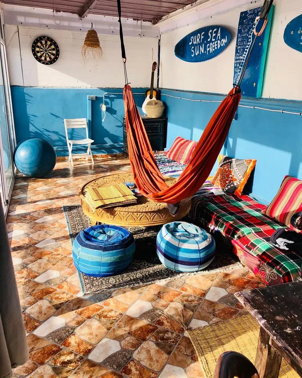 Orange hammock, striped cushions and a carved wooden table in the surf house lounge