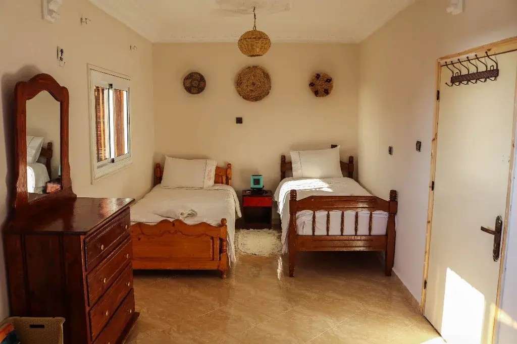 Two wooden single beds in a bright room with woven wall decorations