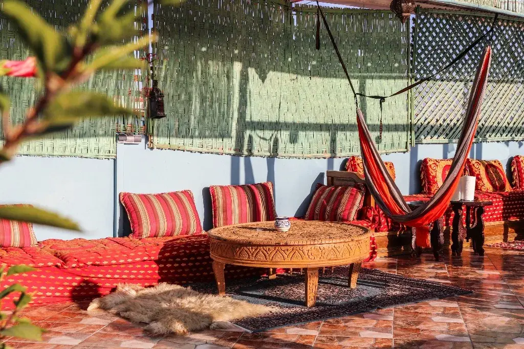 Shaded rooftop lounge with red striped seating, a hammock and a carved round table