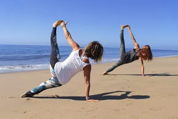 Two people practicing side-plank yoga on the beach beside the ocean